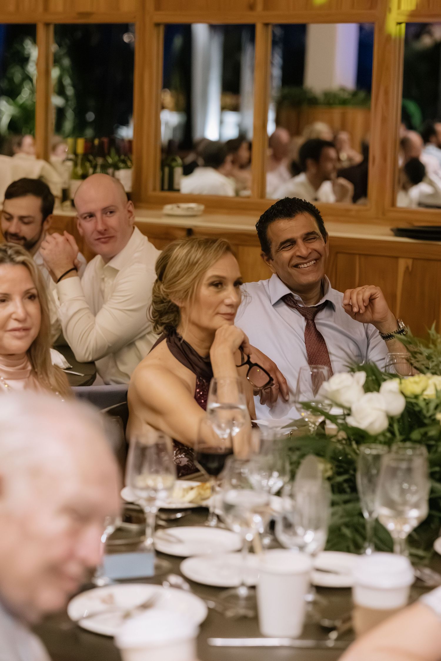 Wedding guests seated at an elegant dinner table with floral centerpieces enjoy the reception celebration.