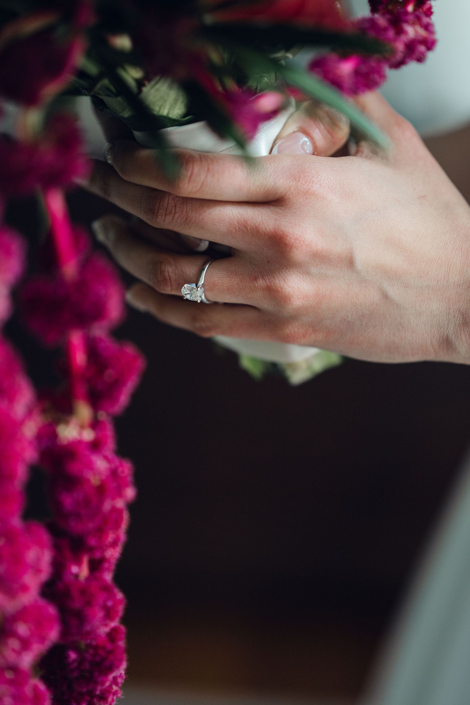 Close-up of a diamond engagement ring on a bride's hand holding a bouquet of vibrant pink flowers.