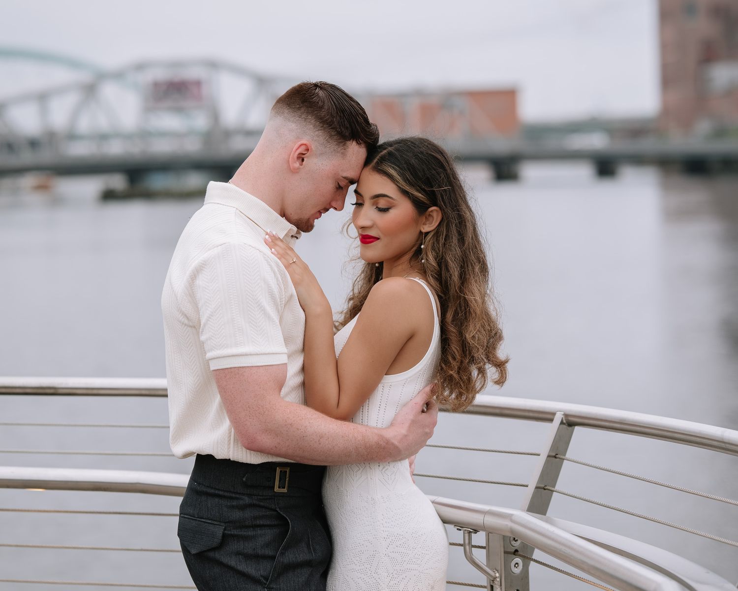 Couple sharing intimate moment by railing overlooking urban waterfront.