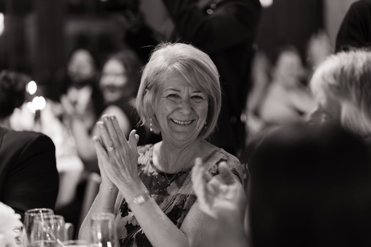 A woman smiling and clapping at a wedding reception in a black and white photo.