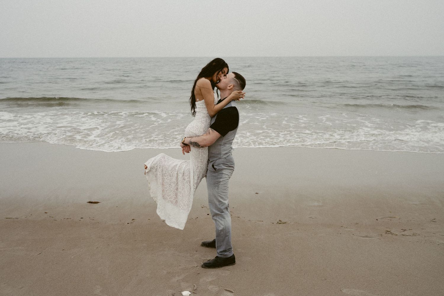 A romantic beach wedding photoshoot with the couple silhouetted against an overcast sky.