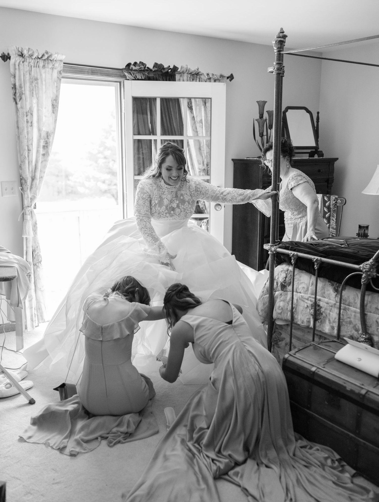 Wedding preparations show attendants helping with a white gown in a sunlit bedroom with vintage decor.