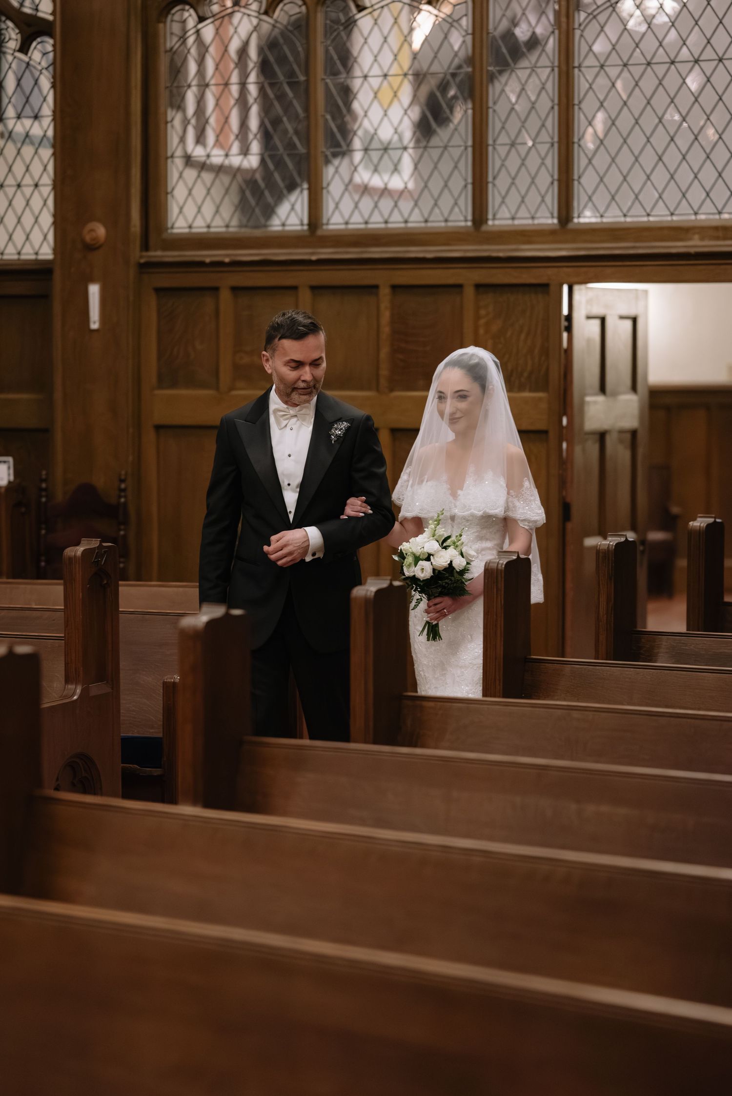 Wedding ceremony inside a traditional church with wooden pews and diamond-paned windows.
