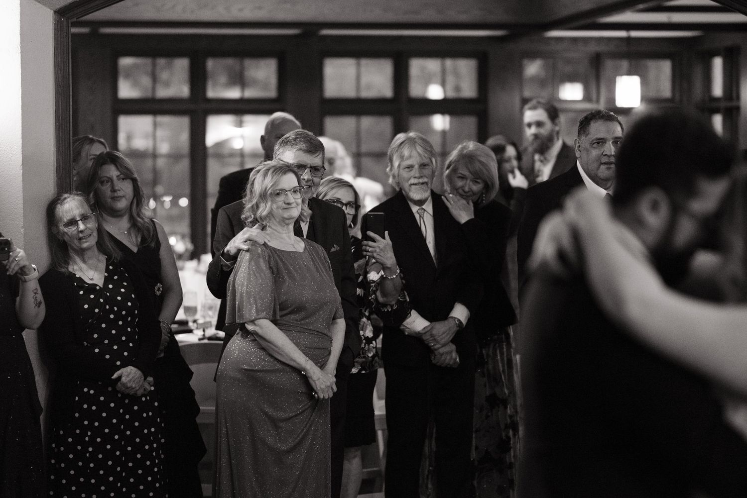 Black and white wedding reception photo showing guests watching couple share first dance in elegant venue.