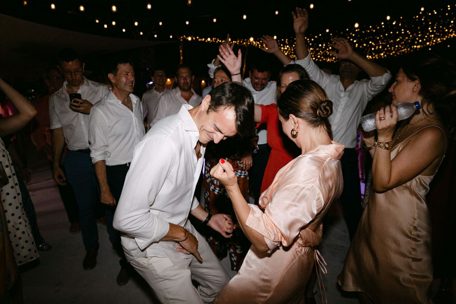 groom and guests dancing during the open-air wedding party of their Spetses wedding, doing an air-guitar motion