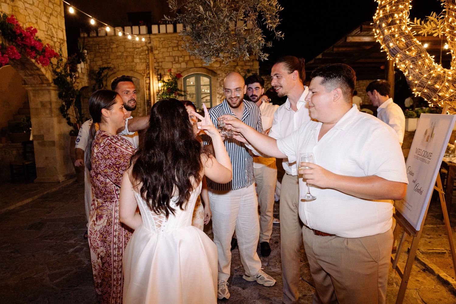 a bride having her back turned on the camera is doing shots with five guests surrounded by fairy lights