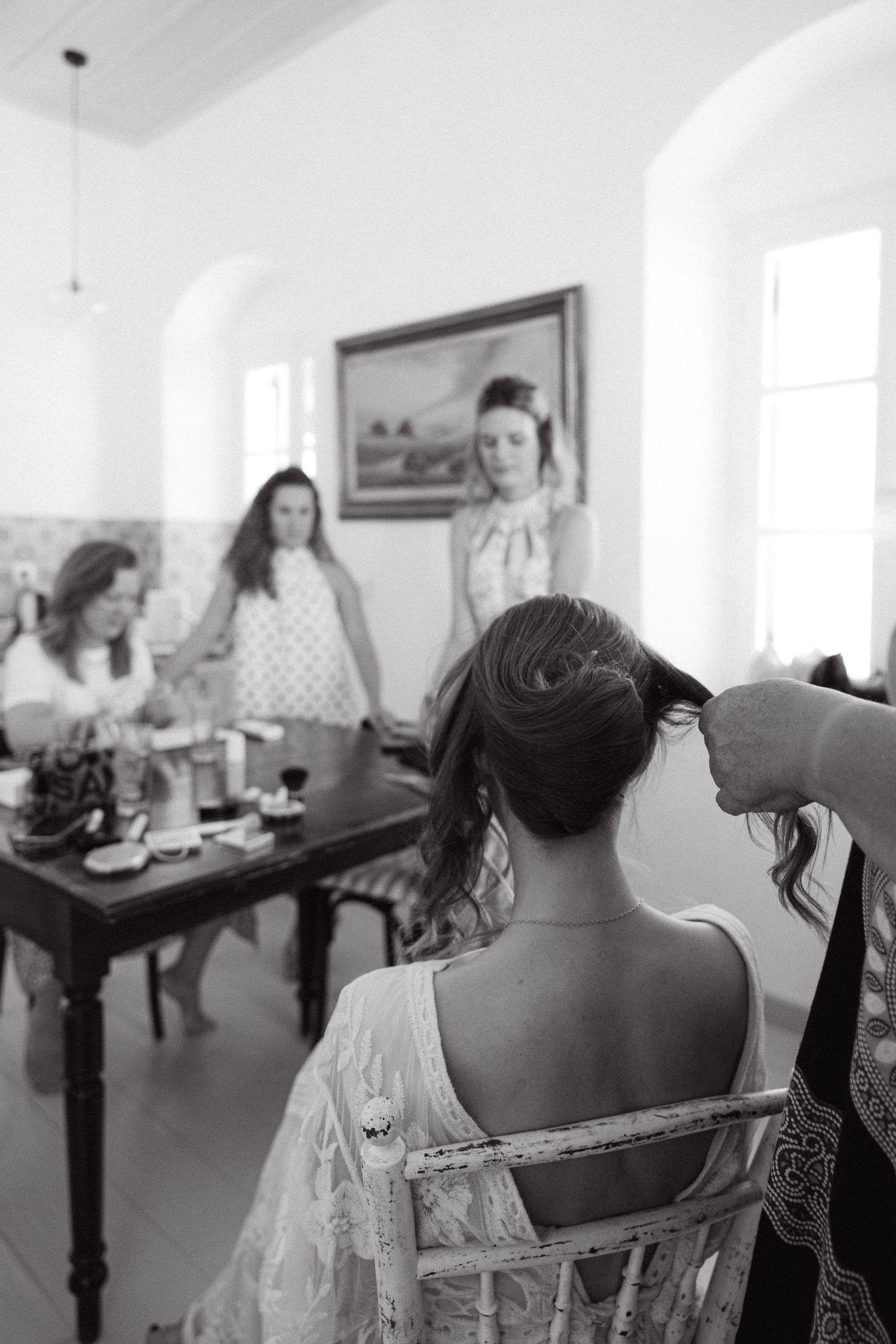 a black and white candind photo taken during a getting ready where the bride sitting in a chair has her hair made with friends