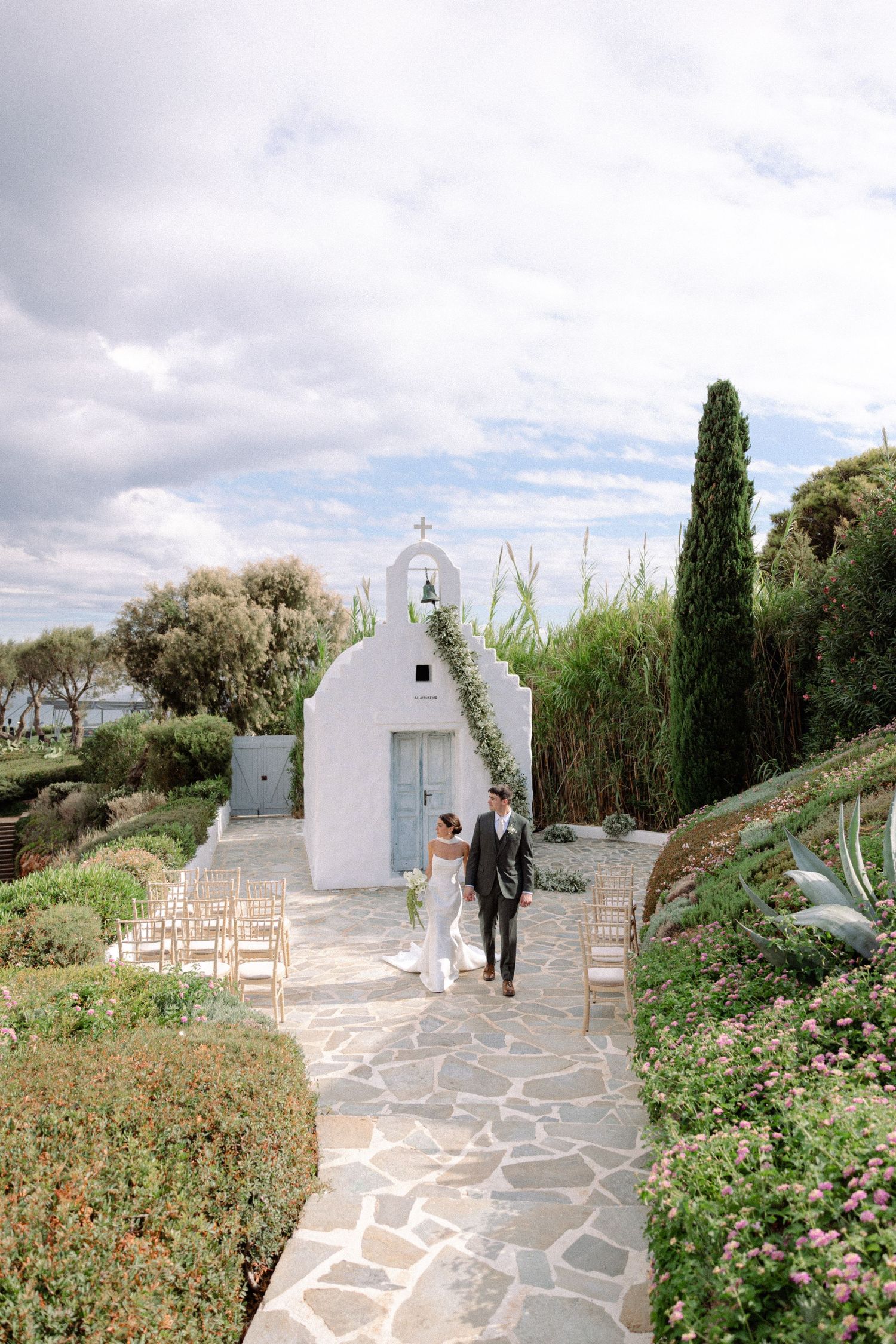 A bride and groom walking hand in hand outside a seaside chapel located in Island Resort Athens Riviera on their wedding day