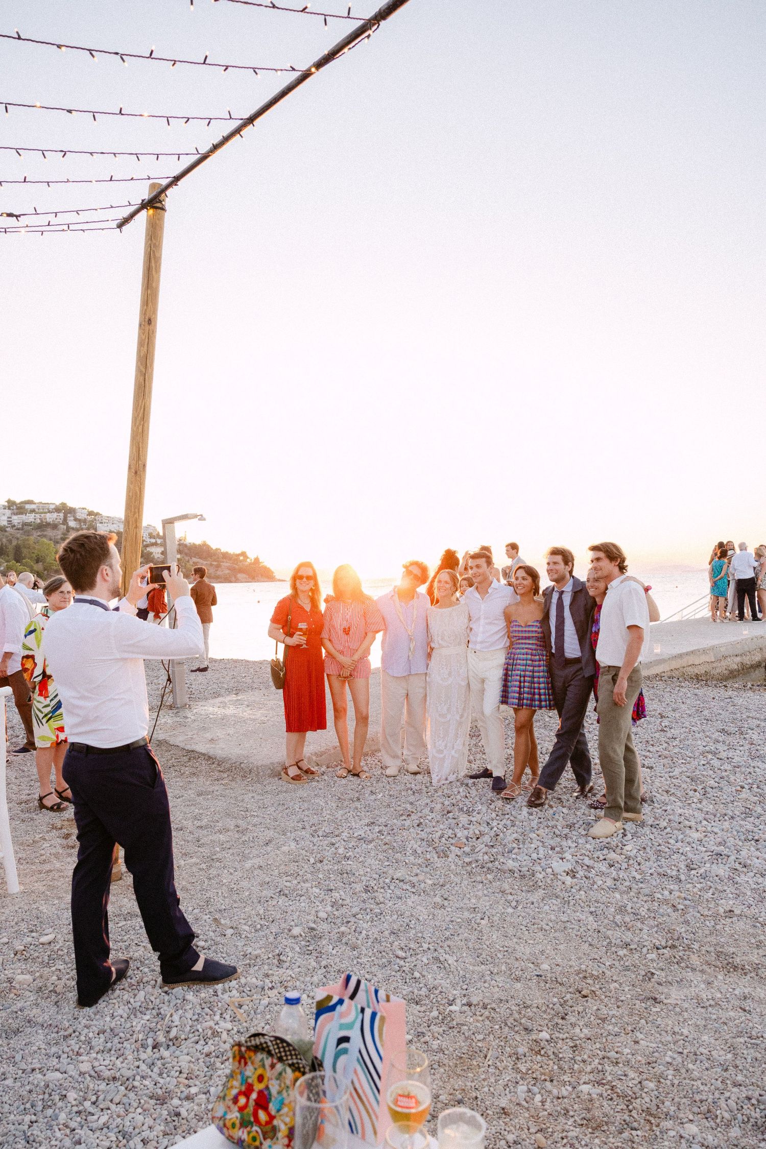 a candid photo from cocktail hour showing a wedding guest taking a group photo of other guests at a beach bar at sunset