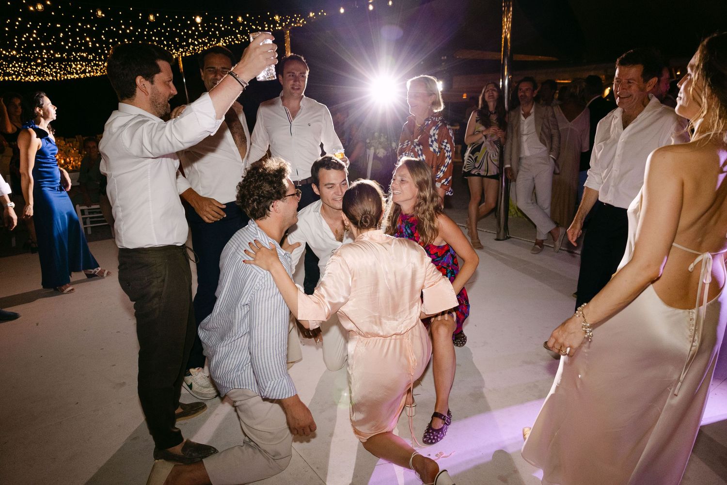 groom and guests dancing during the open-air wedding party of their Spetses wedding, looking at each other and doing the air-guitar