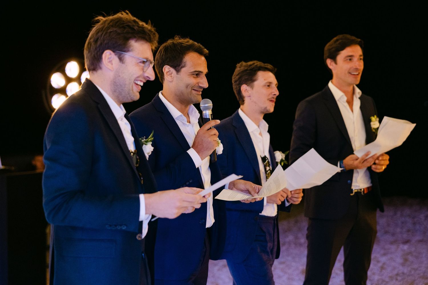 four groomsmen reading speeches from papers they are holding - one of them holds a microphone