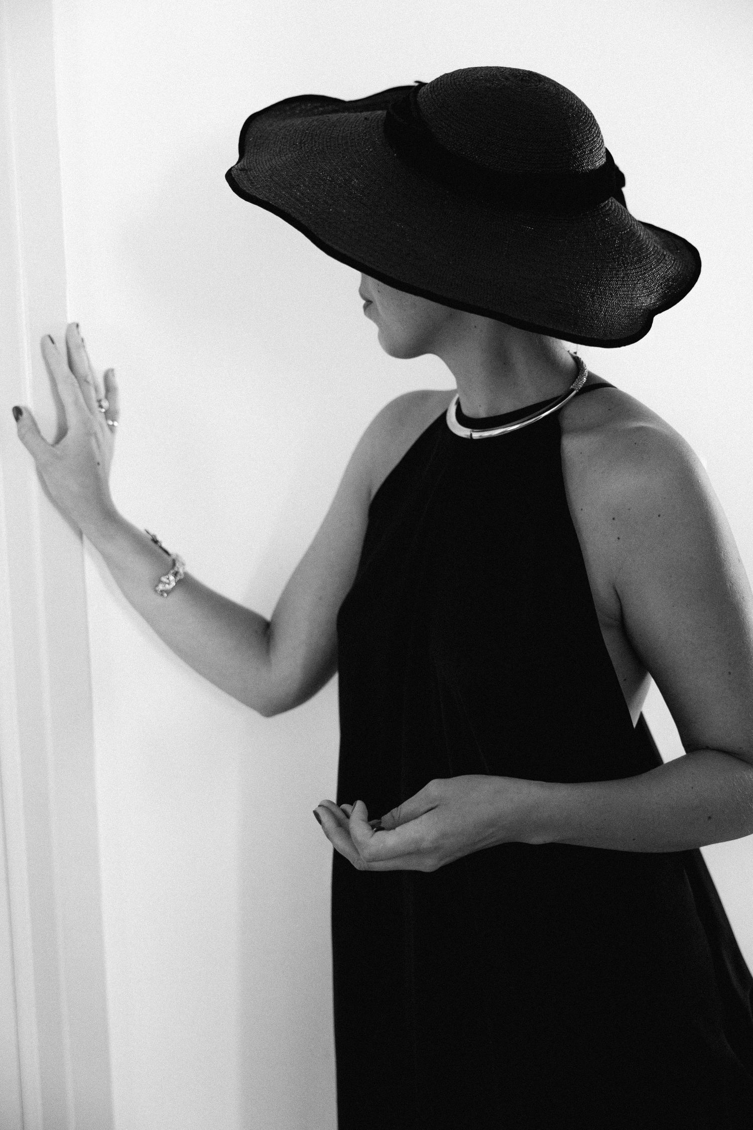 a black and white photo of a woman dressed in black and wearing a black hat against a white background - her face is hidden by the hat