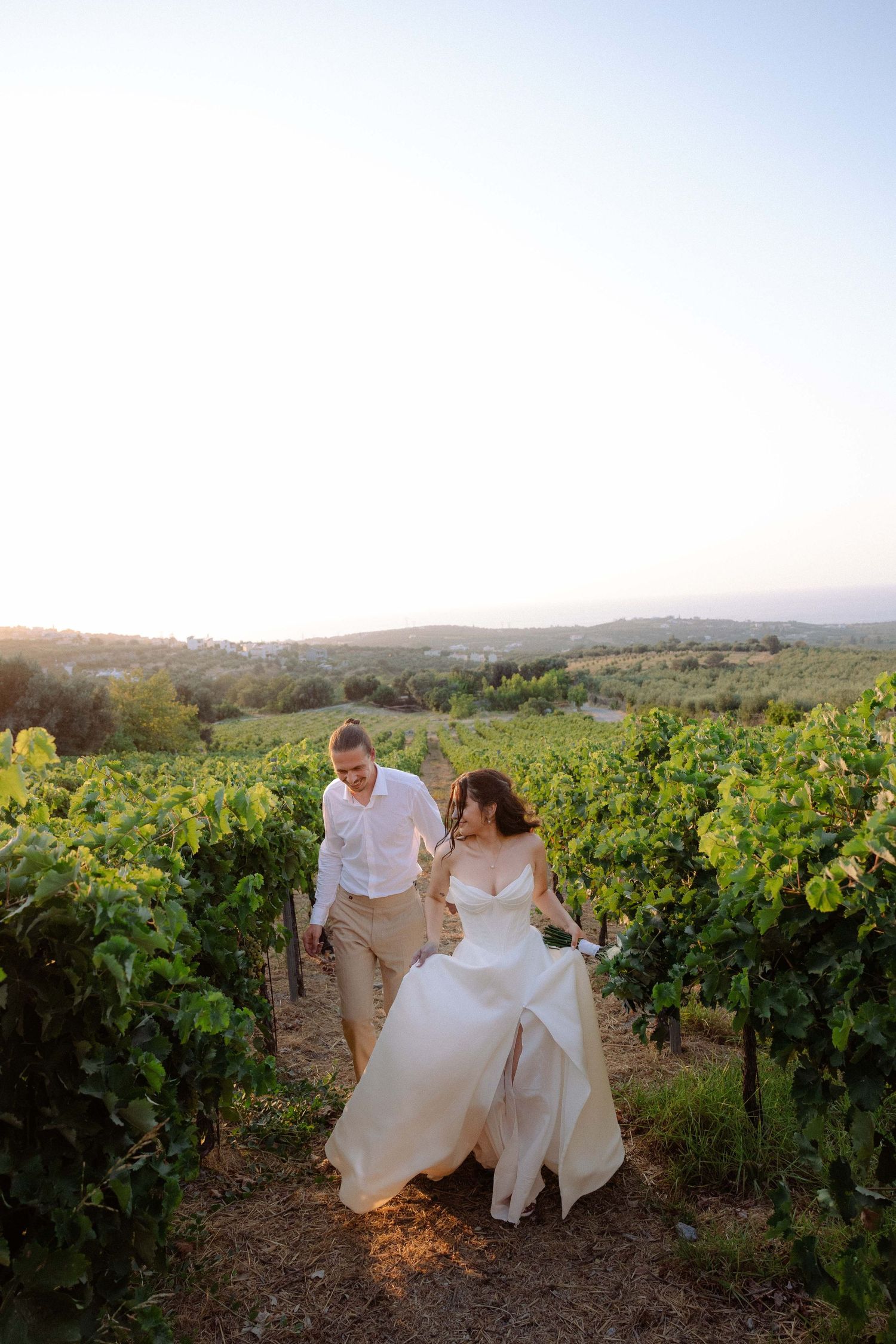 a bride and groom running through a green field while the bride is holding her wedding dress and looks back at him