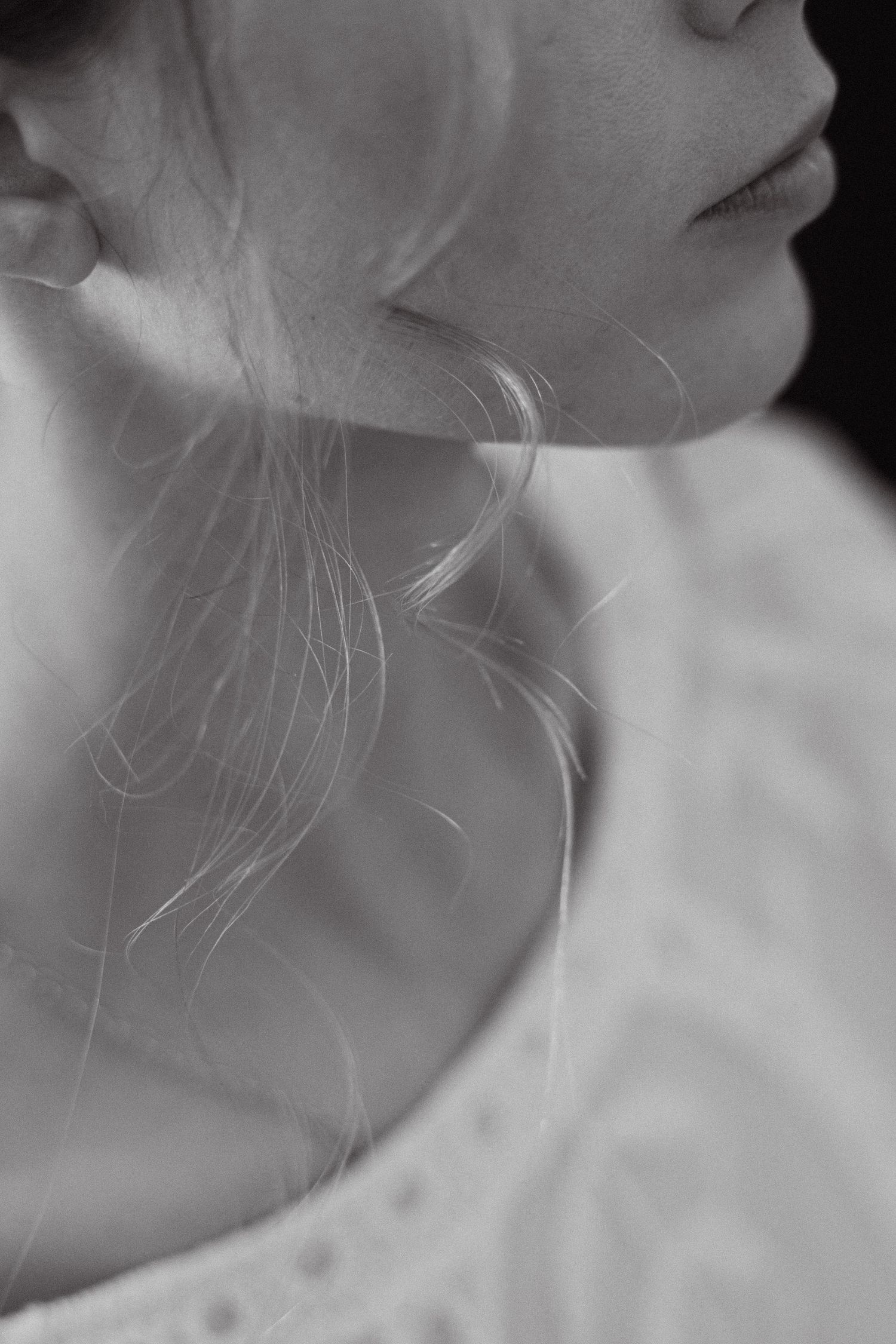 a black and white very close up photo of a woman's lips and neck and a lock of blond hair