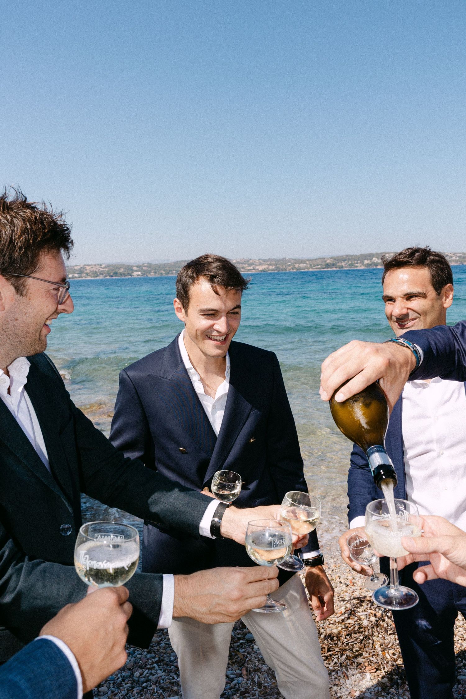 a groom in a beach among groomsmen filling glasses with champagne and smiling