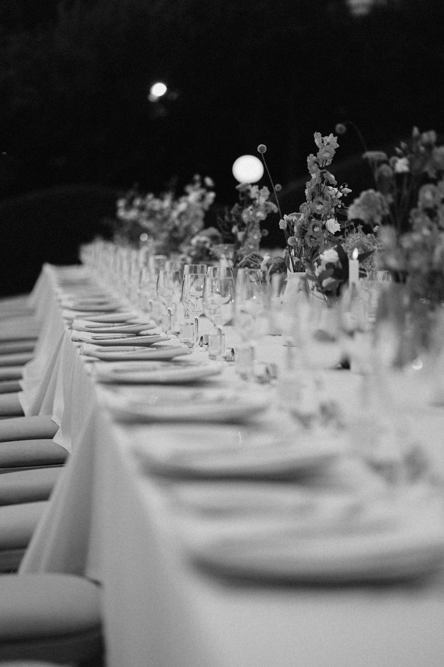 a black and white photo of table set up with plates, glasses and wedding decorations of flowers and candles