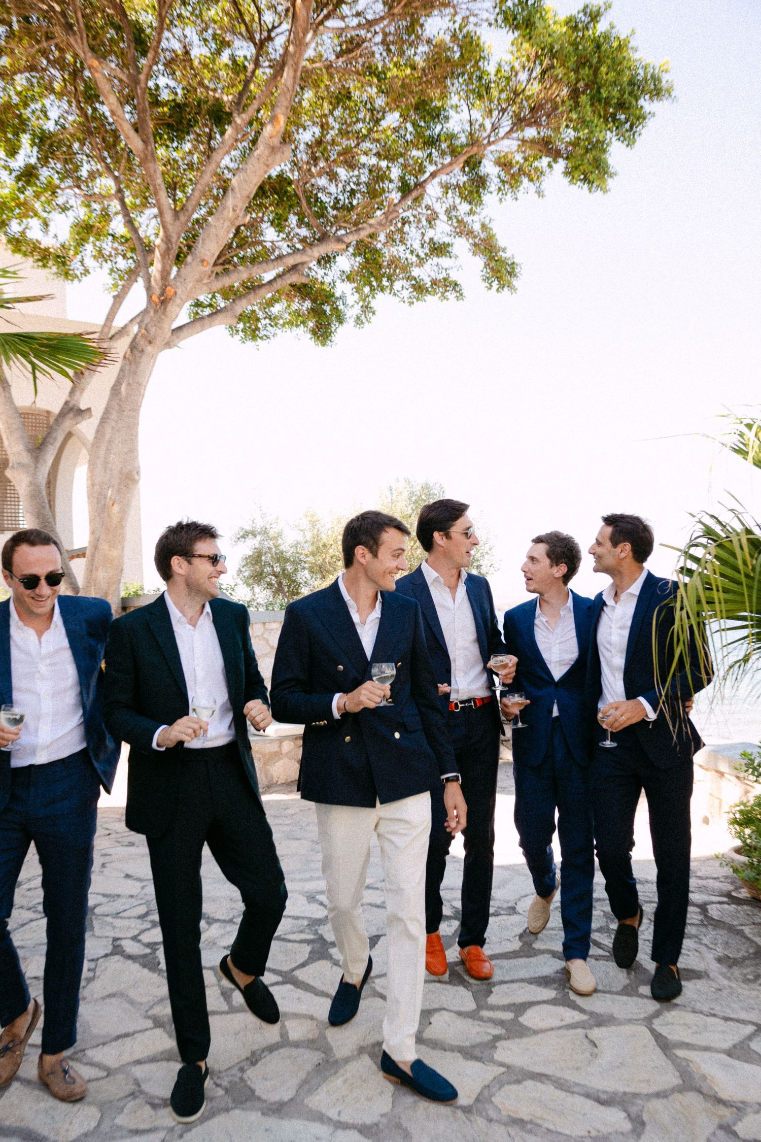 a groom and five groomsmen dressed in matching navy blue suits walking towards the camera and looking at each other smiling and talking