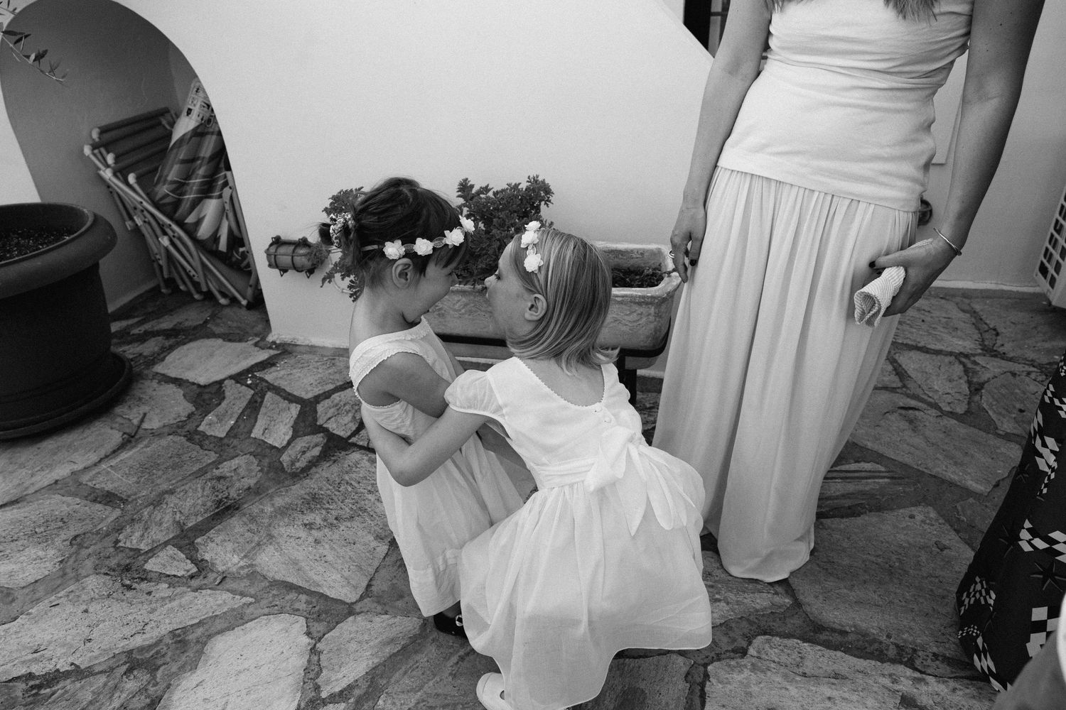 a black and white photo of two kids playing dressed in white dresses and wearing flower crowns and laughing