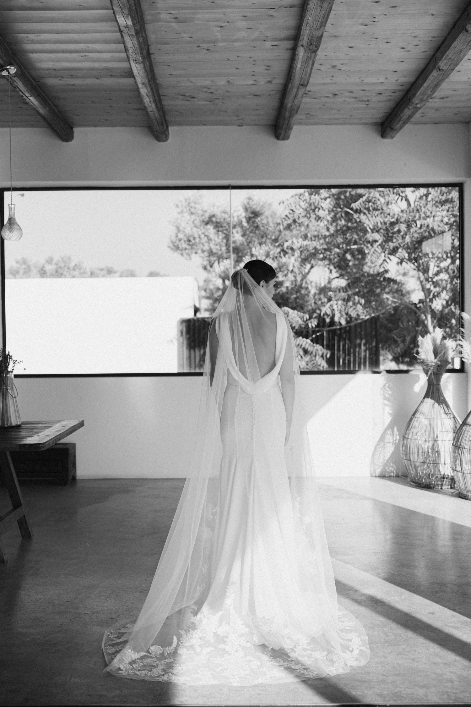 black and white photo showing a bride's back. She is standing in front of a window wearing an open back wedding Dress