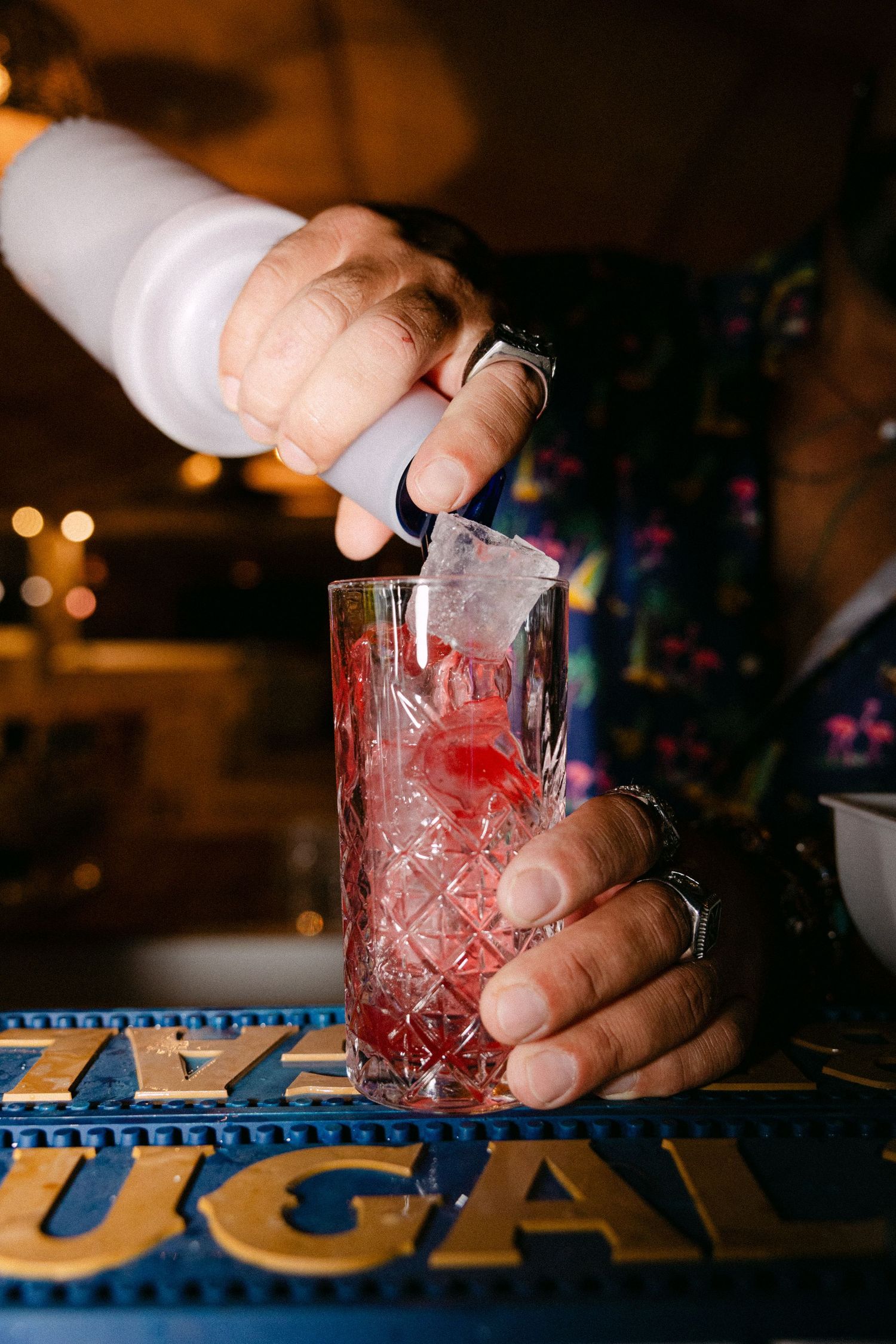 a close-up photo of a red fruity cocktail being prepared as the drink falls into the glass by the barista's hands