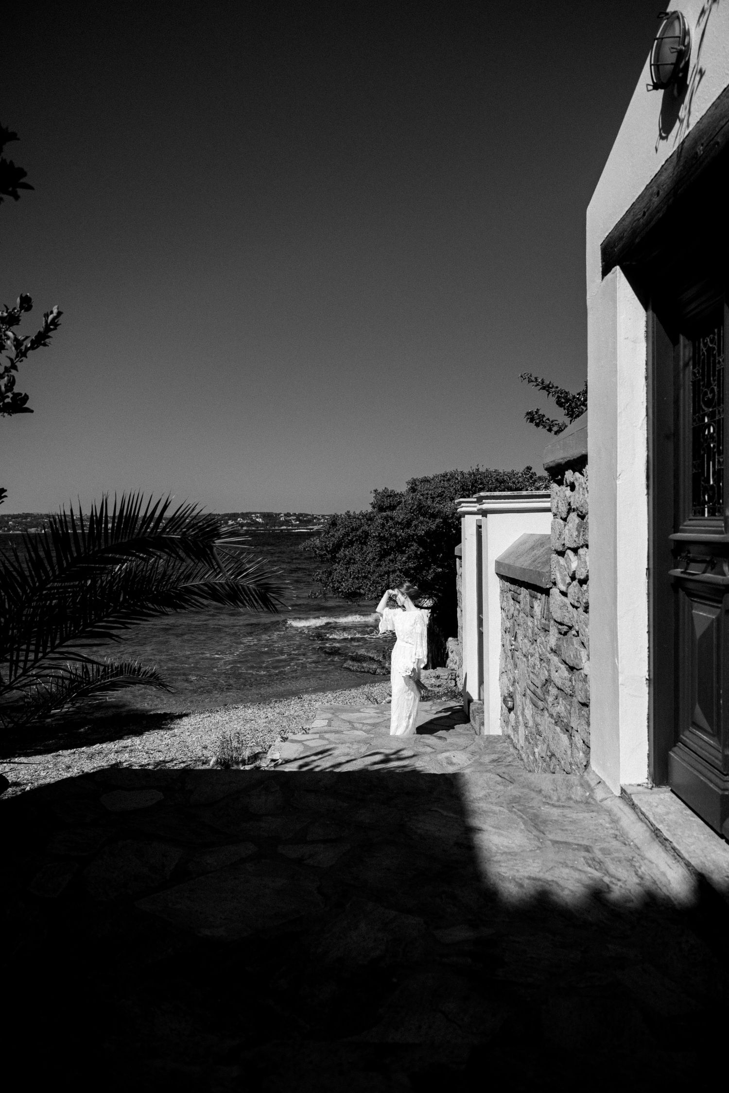 a black and white photo where a bride is visible far away in high-contrast lighting with harsh sun, shading her eyes with her hand