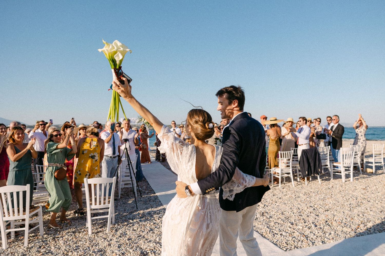a bride and groom hugging with their backs on the camera cheering after their wedding ceremony facing the guests