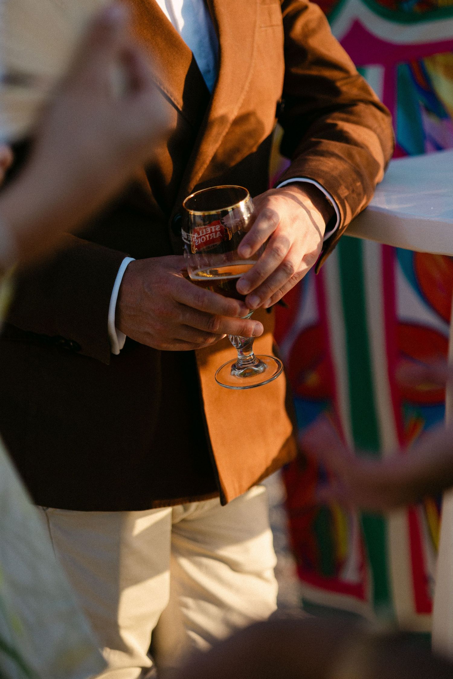 a close up of a wedding guest's hand holding a wine glass with wine - he is wearing a brown suit
