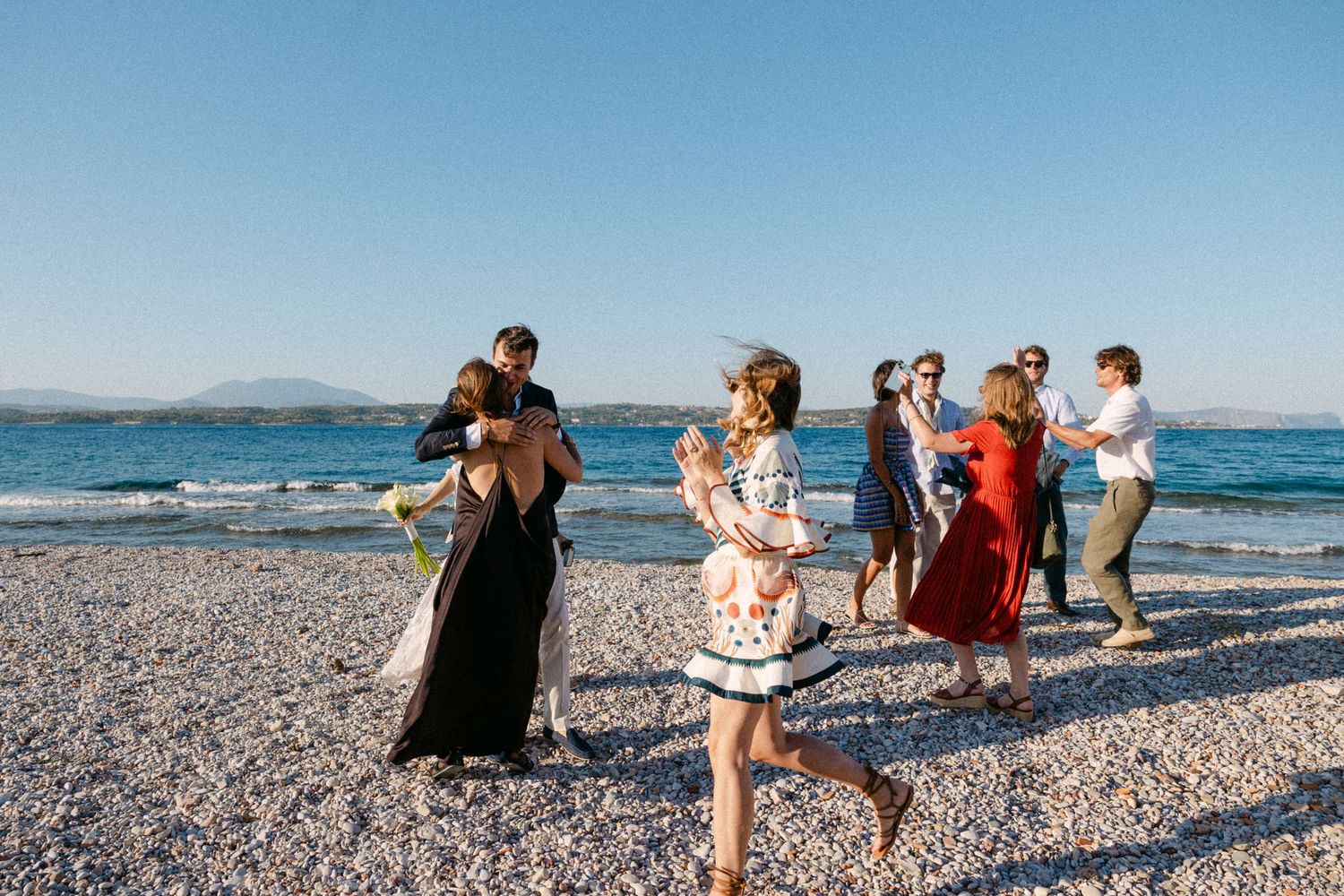 wedding guests hugging at the beach at early afternoon and a woman is running