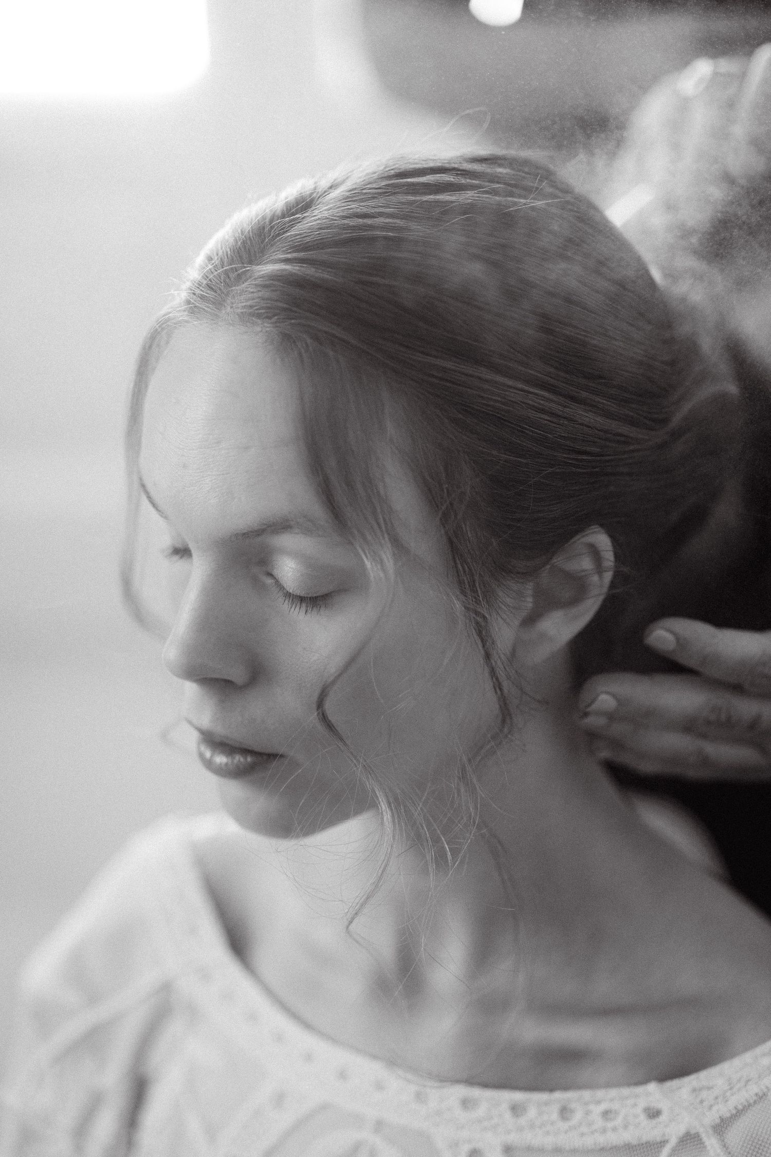 a black and white close-up portrait of a person being sprayed hair spray while having closed eyes