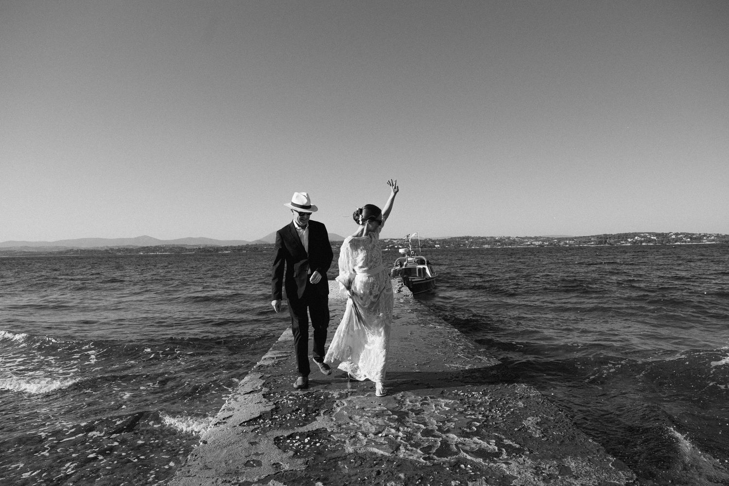 a black and white photo of a bride and her dad walking in a dock, while the bride is waving