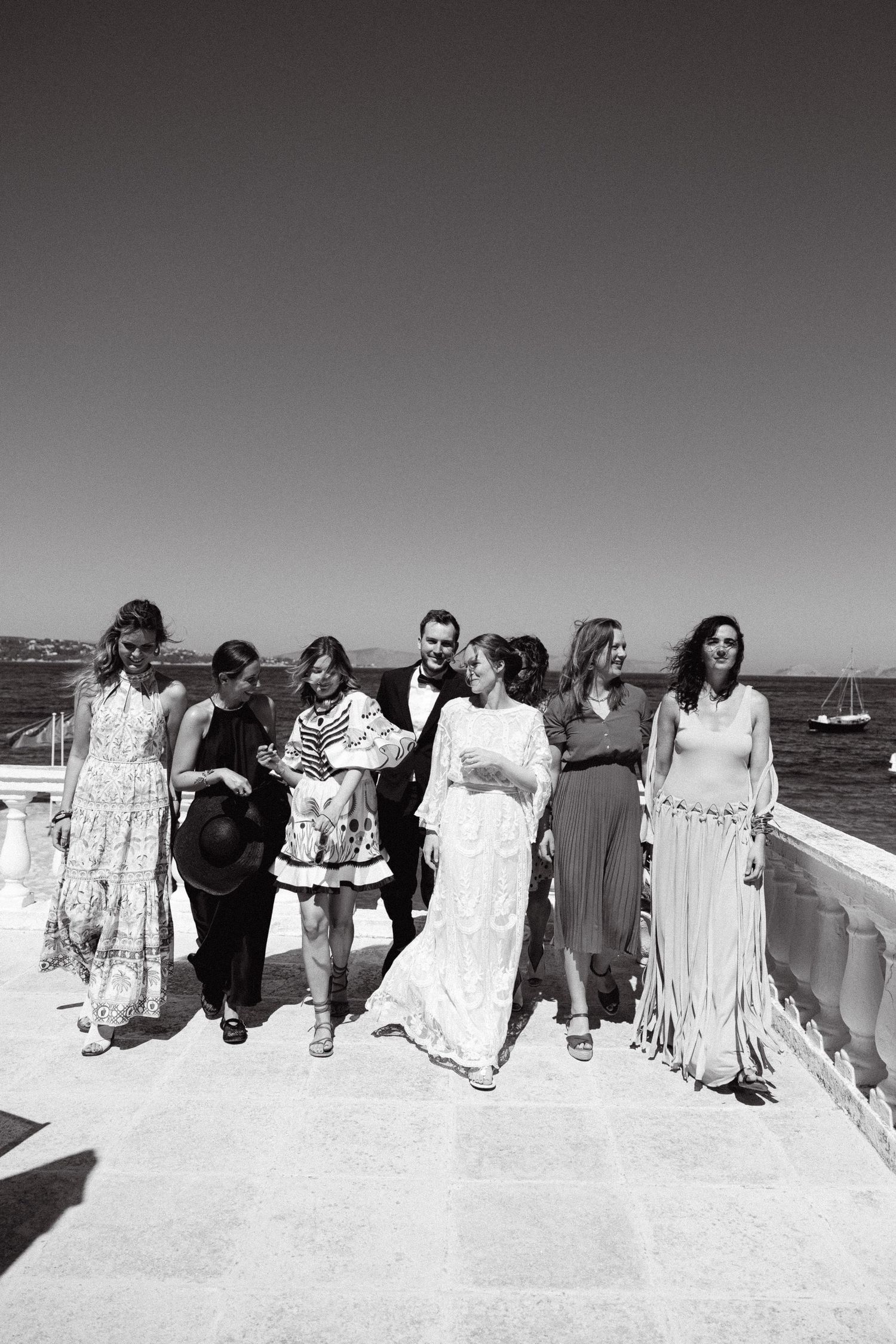 a black and white photo of a bride and her friends in a terrace, walking towards the camera and smiling at each other