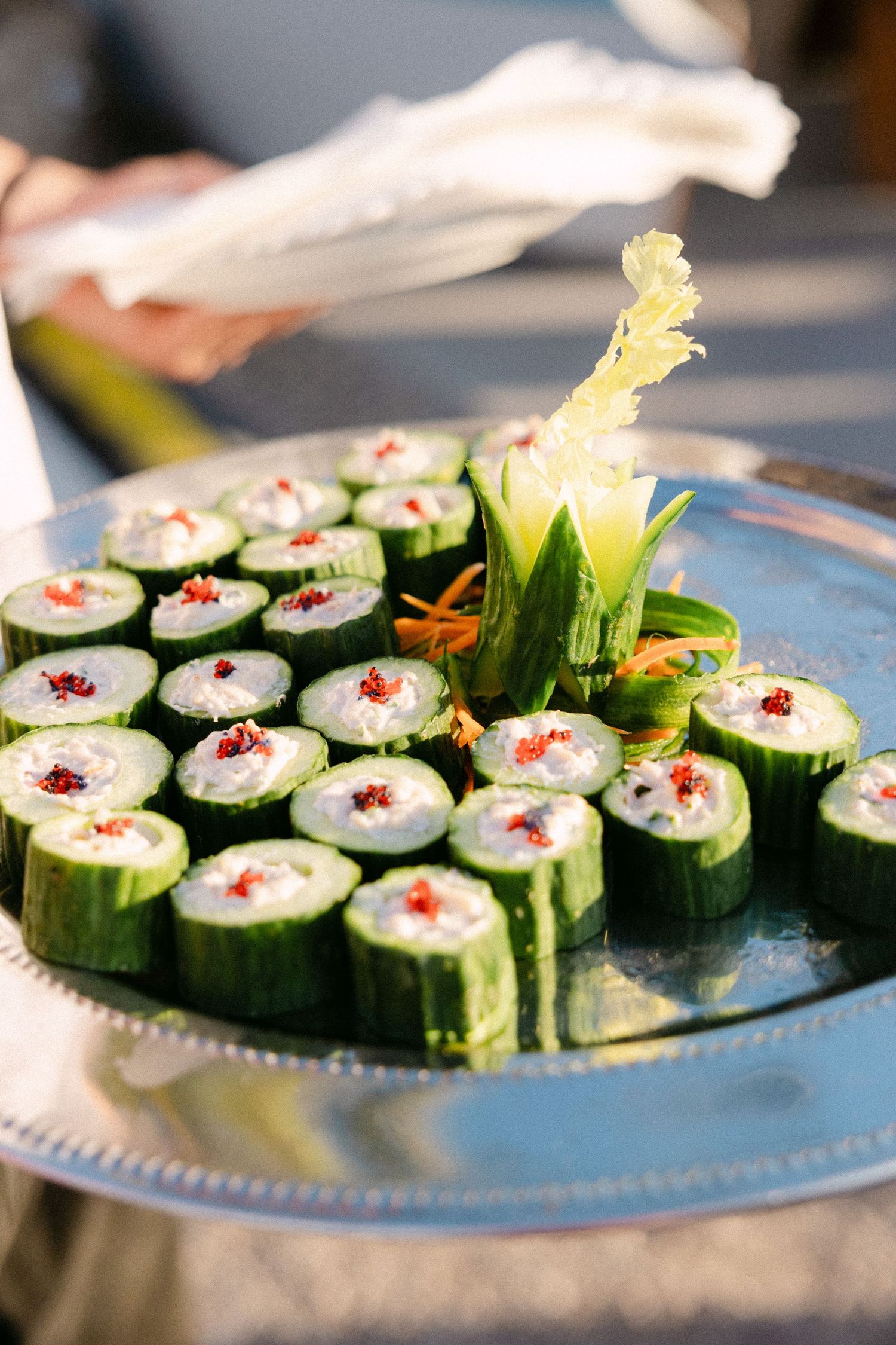 a close-up photo of an entree dish that is sushi-like rolls of cucumber on a silver plate being held by the waiter's hands