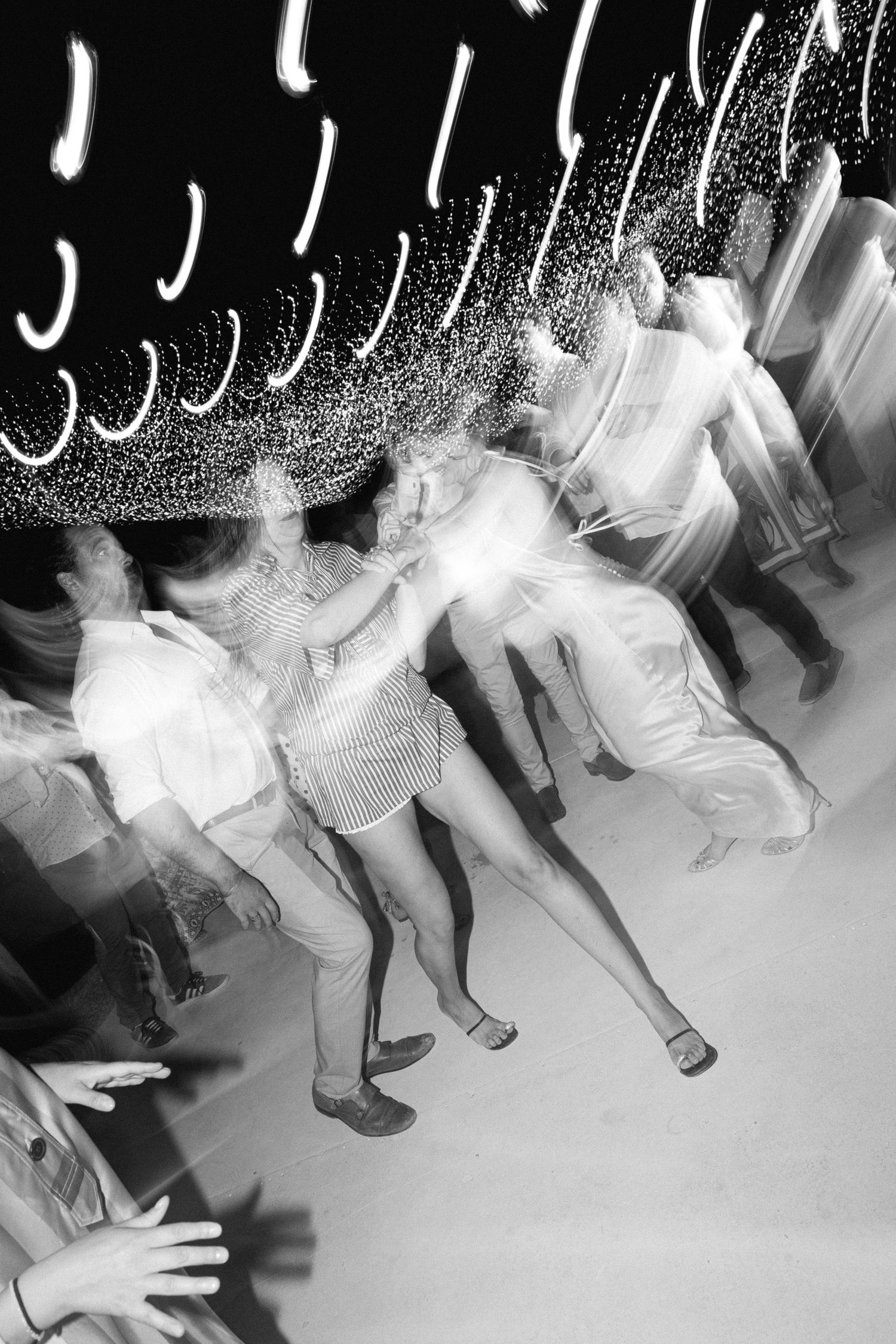 a black and white motion blurred photo of guests dancing under carnival lights in an open air wedding party in spetses, Greece