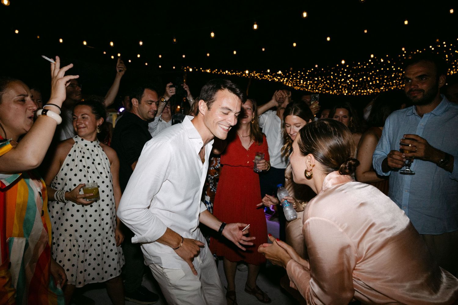 groom and guests dancing during the open-air wedding party of their Spetses wedding, doing an air-guitar motion