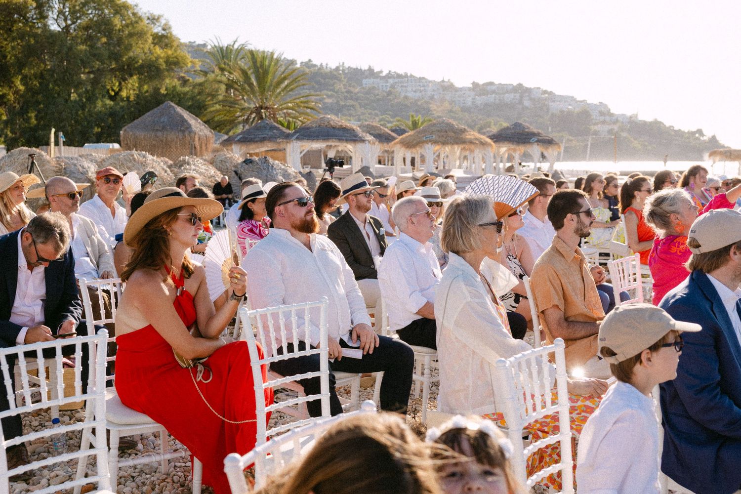 a wide photo of wedding guests sitting in chairs during a sunny open-air wedding ceremony