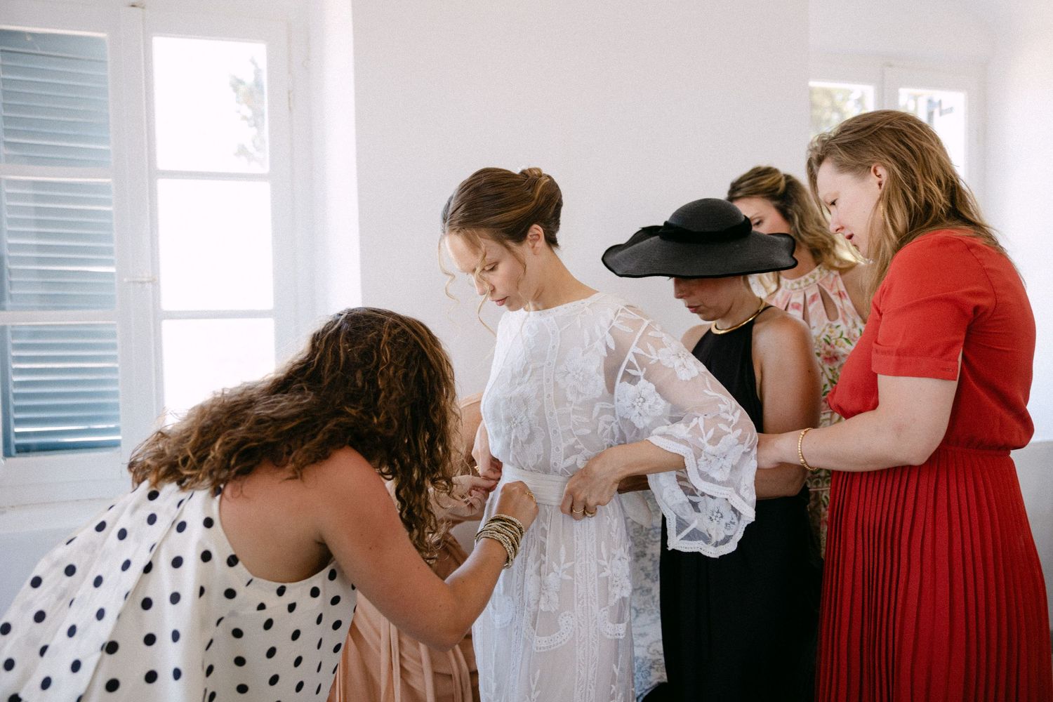 a candid photo of a bride being dressed by her four girlfriends - they are fixing the belt of her wedding dress