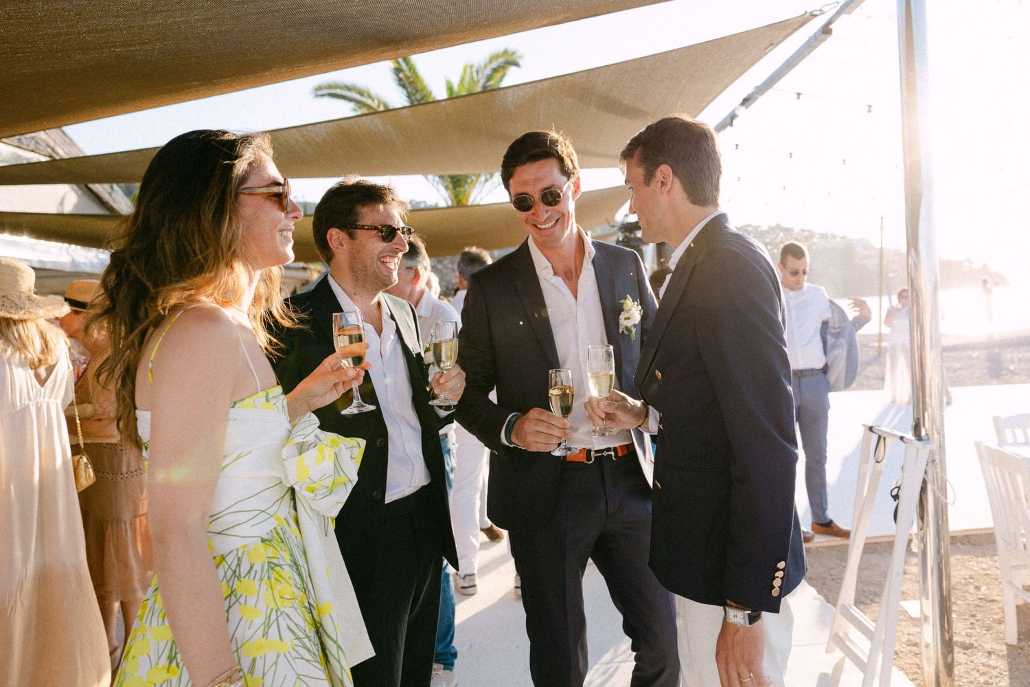 four guests casually conversing during a wedding's cocktail hour at a beach club in Greece