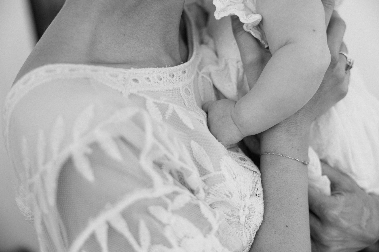 a black and white close-up photo of a baby's hand touch a woman's chest while she is holding it