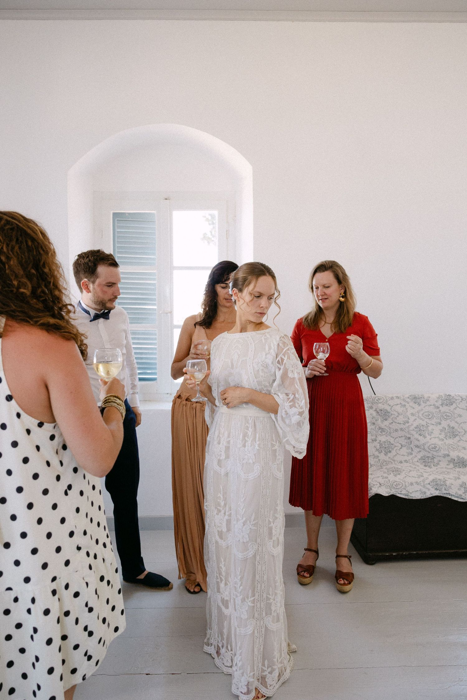 a bride calmly looking down, surrounded by friends in a spetses summer house