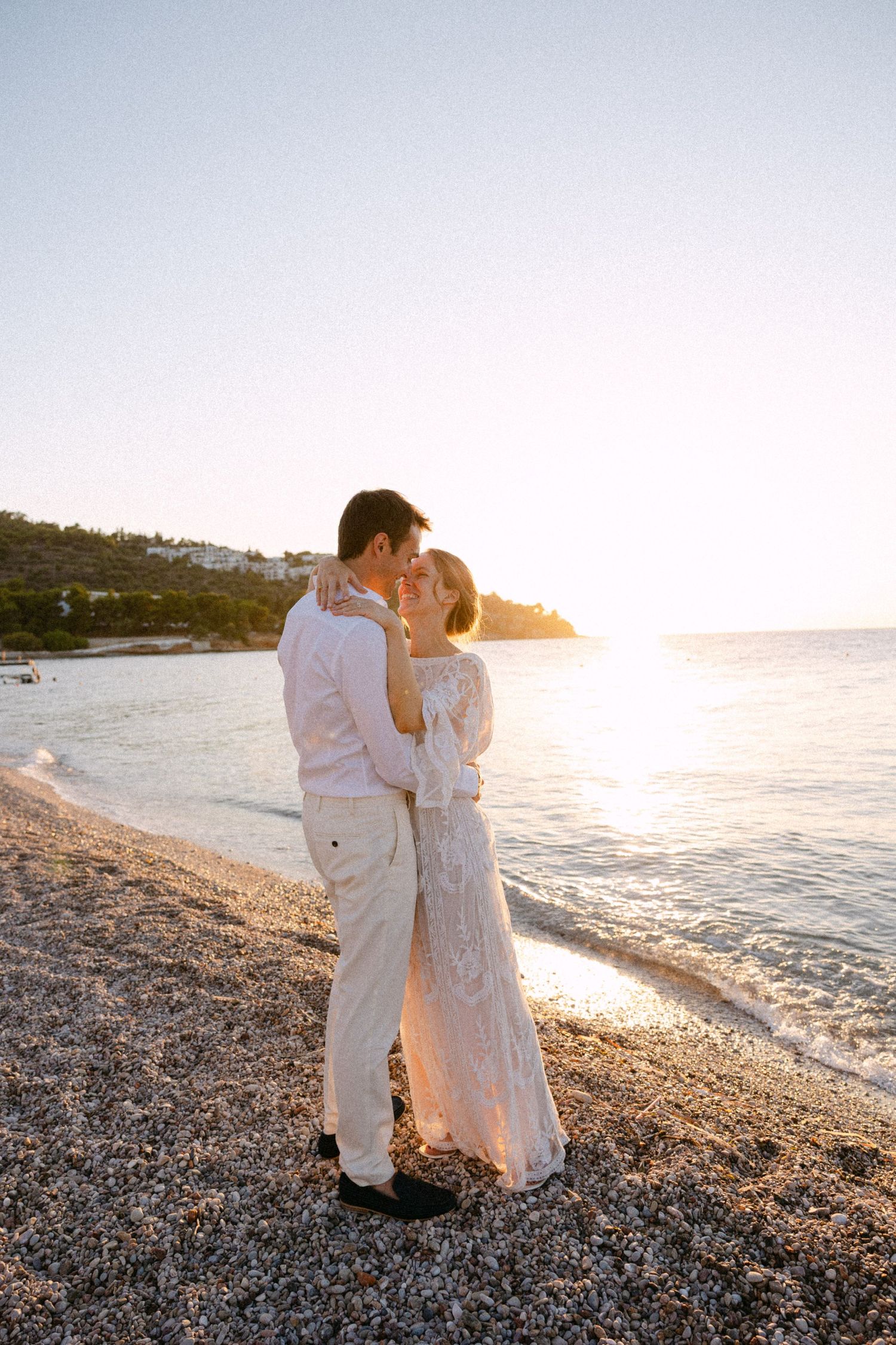 a bride and groom kissing in a greek beach at sunset