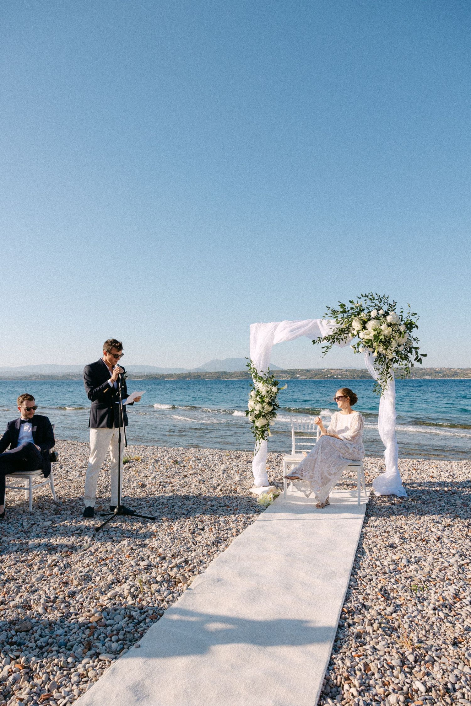 a groom reading his speech into the microphone while looking at the bride during their beach ceremony