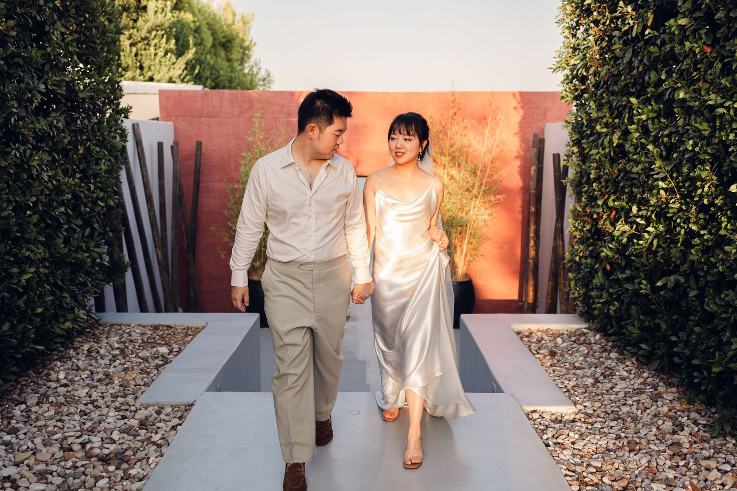 a bride and groom walking as they are holding hands at sunset with their wedding venue building as a backdrop