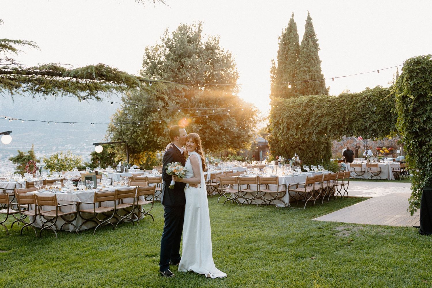 A newlyweds portrait after the ceremony. The groom is kissing the smiling bride's cheek in the reception area during sunset