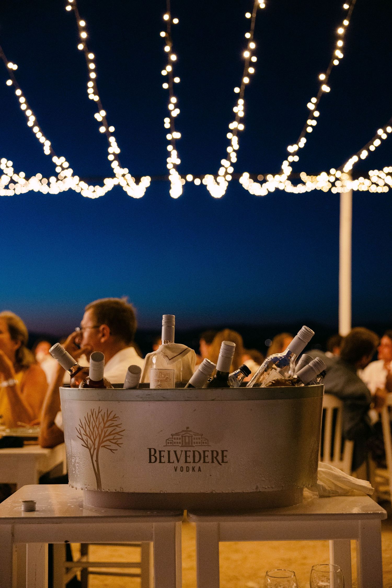 a bucket of ice-cold wine bottles against a background of a wedding reception in a beach bar