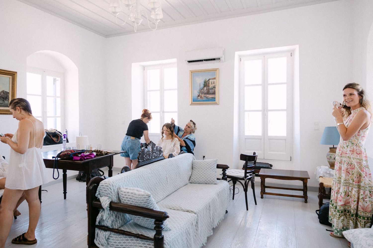 a white room where women are getting ready - some are having their har done, other are putting on earrings. The house is mostly white.