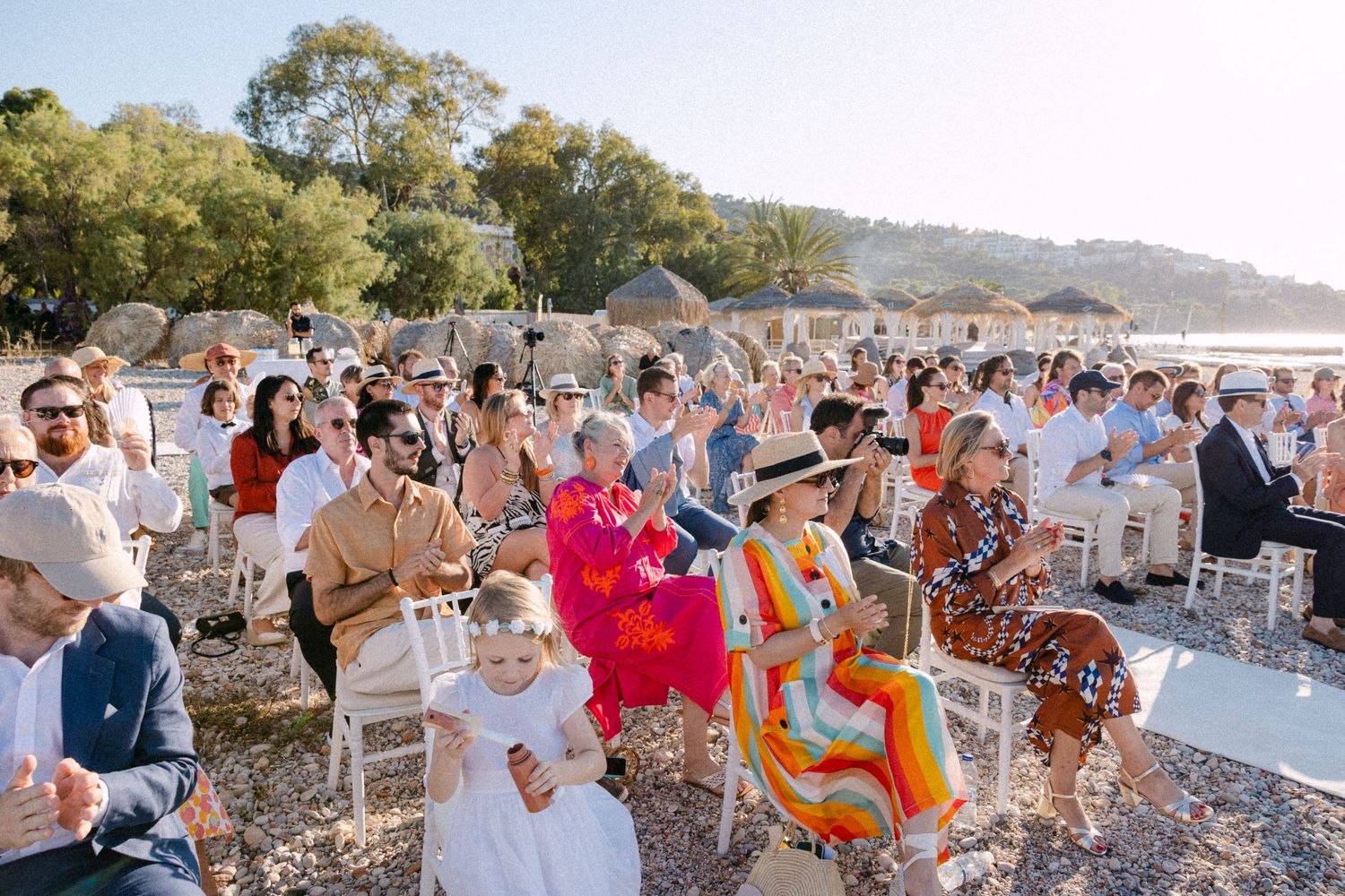 a wide photo of wedding guests sitting in chairs during a sunny open-air wedding ceremony