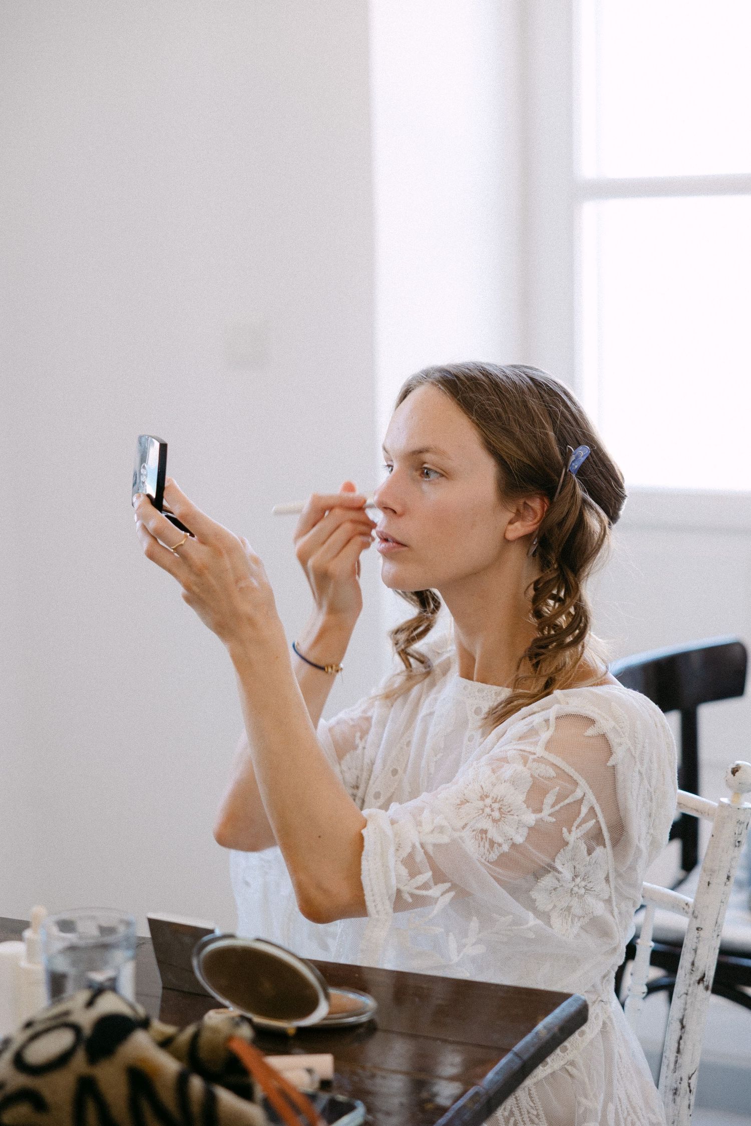 a bride doing her own make up and putting blush on while her hair are help by bobby pins during her getting ready in a white room