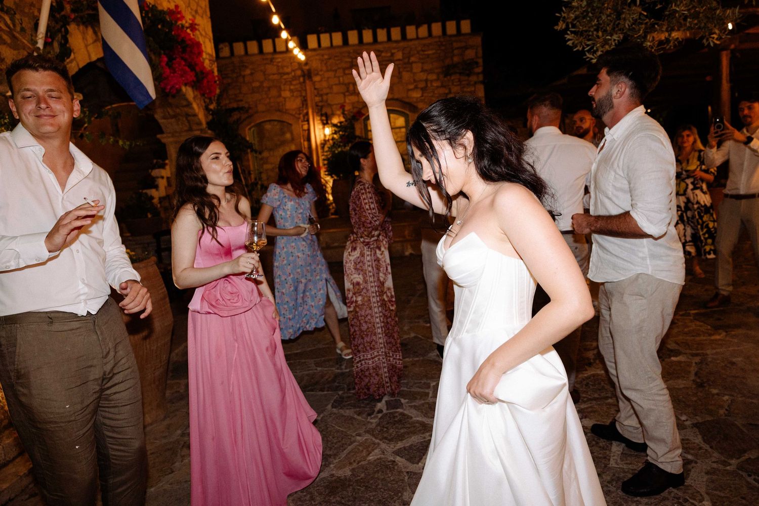a bride dancing with hands up in the air among other people dancing at night