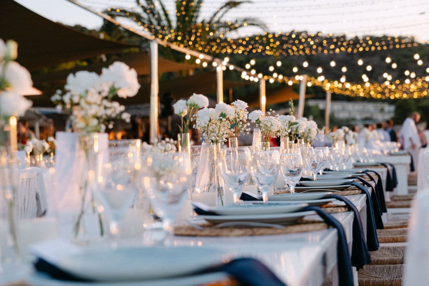 wedding table decorations showing white flowers in a vase, a lit candle and blue plates and glass wines