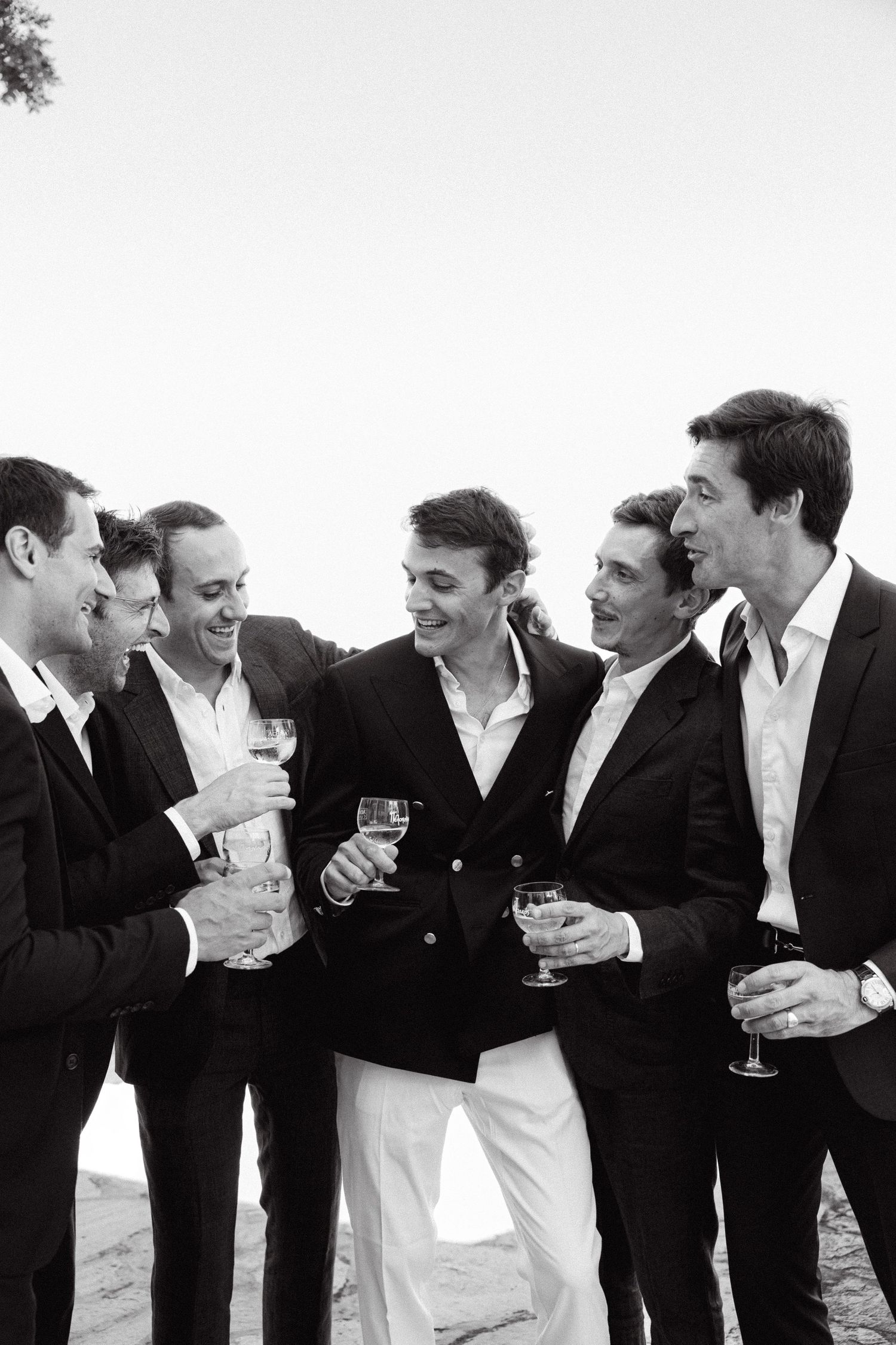 a black and white photo of a groom among groomsmen smiling and holding glasses of champagne
